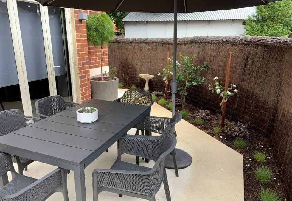 Front garden with paved patio, grey outdoor table, chairs and parasol