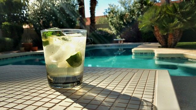 Best plants for around pools. Image of a cocktail next to a pool surrounded by plants